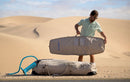 Rider che tira fuori una sacca singola Duotone accanto a una borsa con ruote nel deserto, collezione Boardbag Single Compact 2027