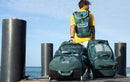 Rider de espaldas con mochila y bolsas de viaje Duotone verdes en un muelle, colección Boardbag Single Surf 2027