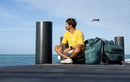 Rider sentado en un muelle junto a sus bolsas de viaje Duotone verdes, colección Combibag 2027