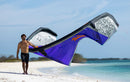 Rider en la playa sujetando la cometa Duotone Dice SLS 2027 en gris y morado