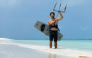 Rider en la orilla de una playa tropical con su twintip con fijaciones Duotone Entity 360 2027