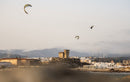 Rider che saltano con il kite Duotone Rebel D/LAB 2025 davanti a una città costiera con le montagne sullo sfondo