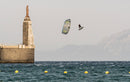 Rider che salta con il kite Duotone Rebel D/LAB 2025 vicino a un molo di pietra con una statua