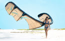 Rider che cammina sulla spiaggia con in mano il kite Duotone Rebel SLS 2026 (versione colorata) da 10 m