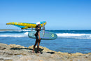 Rider con la wing Unit D/LAB y la Duotone Skybrid SLS 2027 caminando por la costa rocosa