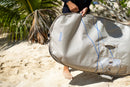 Rider sacando la funda Duotone Wing Boardbag Mid-length 2027 color marfil en la arena de la playa