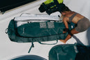 Rider guardando el equipo en la funda Duotone Wing Boardbag Mid-length 2027 verde en la cubierta de un barco