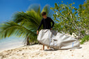 Rider sujetando la funda Duotone Wing Boardbag Single 2027 marfil junto a una palmera en la playa