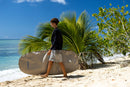 Rider caminando por la orilla con la funda Duotone Wing Boardbag Single 2027 marfil bajo el brazo