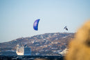 Rider saltando alto con la cometa North Orbit 2027 Deep Purple frente a una costa con pueblo blanco