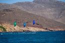 Tres riders navegando con la North Orbit 2027 en Super Lime, Turquoise y Deep Purple junto a una costa rocosa
