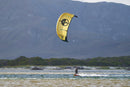 Rider navegando con la North Reach 2025 Sunset Yellow junto a la playa con montañas al fondo