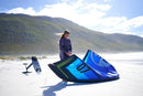 Rider preparando en la playa la North Reach 2025 Pacific Blue junto a una tabla de foil