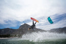 Rider in salto con il kite North Reach 2026 Turquoise sull'acqua davanti alla montagna