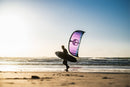 Rider che cammina sulla riva con la tavola da surf e il North Reach 2026 Deep Purple al tramonto