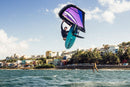 Salto con wing morada y la North Swell Pro frente a una ciudad costera